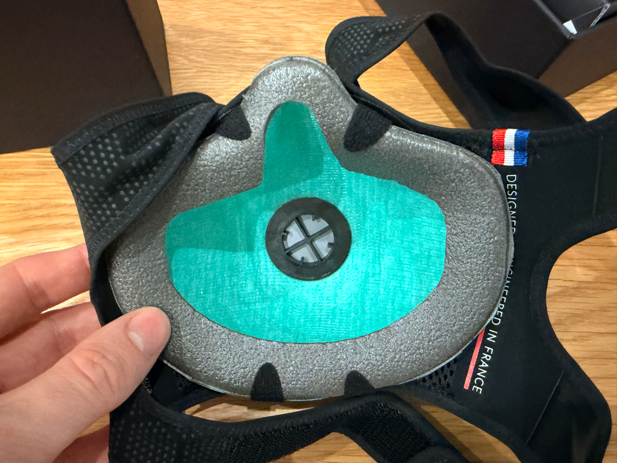 Intérieur d'un masque avec filtre, couleur turquoise, tenu par une main sur fond en bois.