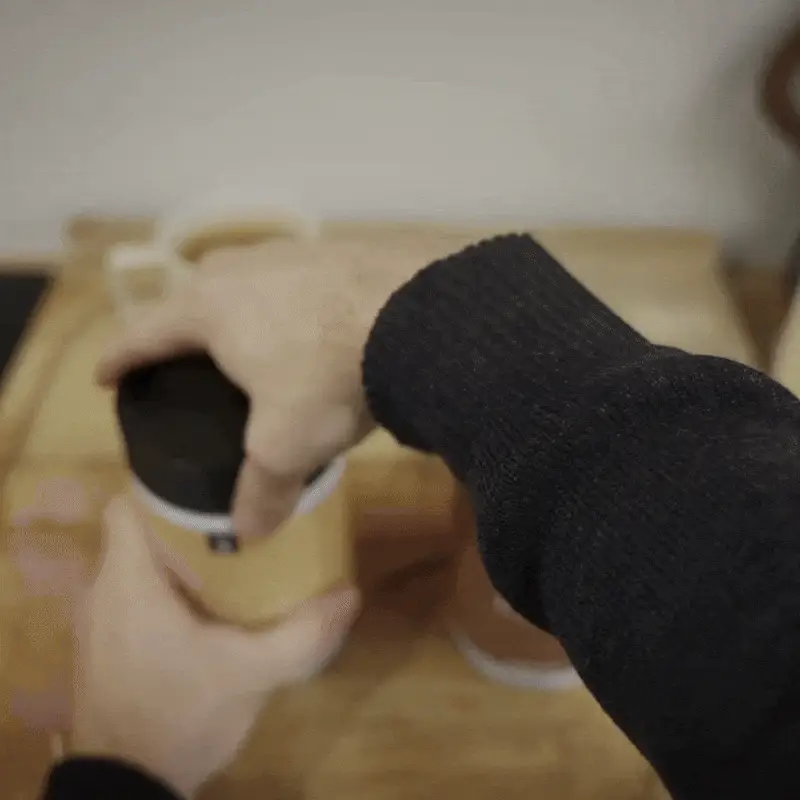 Main soulevant le couvercle d'un contenant en bois sur une table en bois.