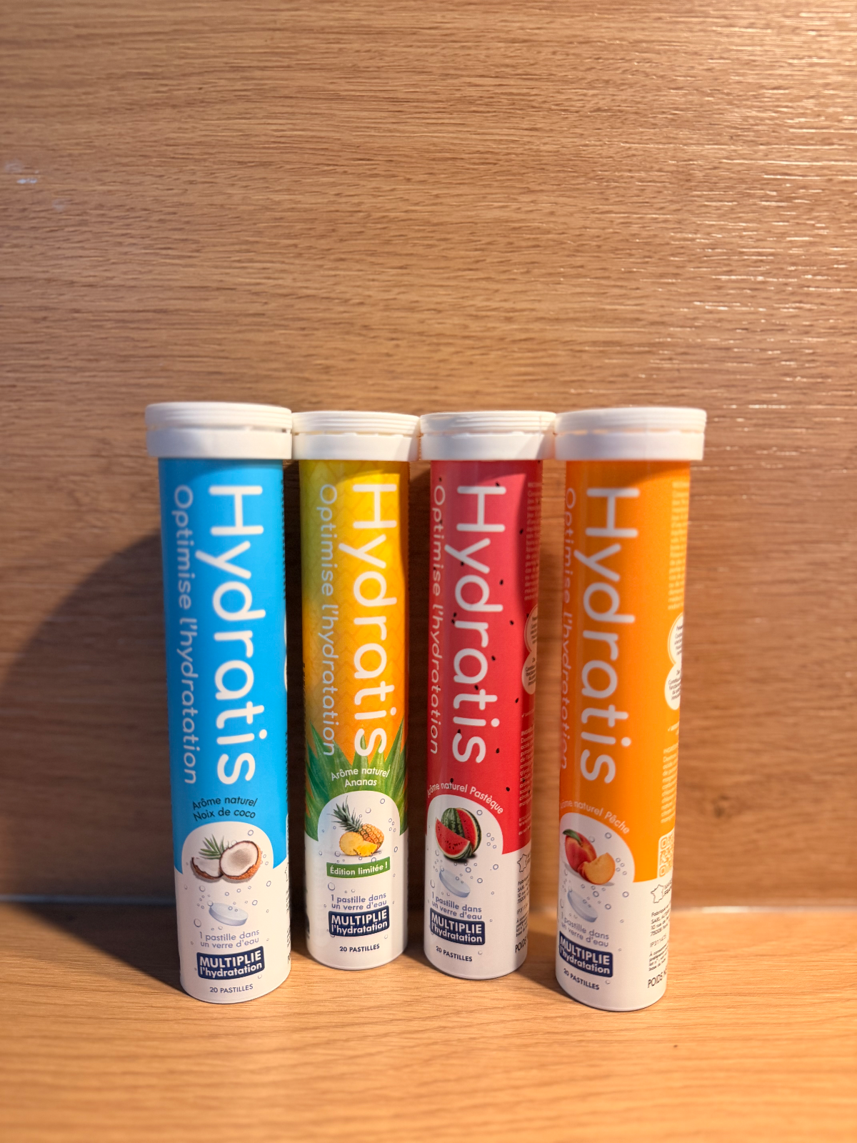 Quatre tubes de pastilles Hydratis de saveurs variées sur fond en bois.